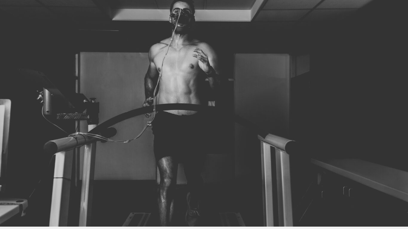 A runner is running on a treadmill wearing a facemask for an maximal oxygen uptake test, running in shorts only with no shirt.